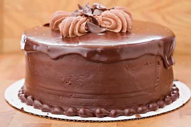 A straight close up shot of a whole chocolate fudge cake. Photographed against a  wooden background.