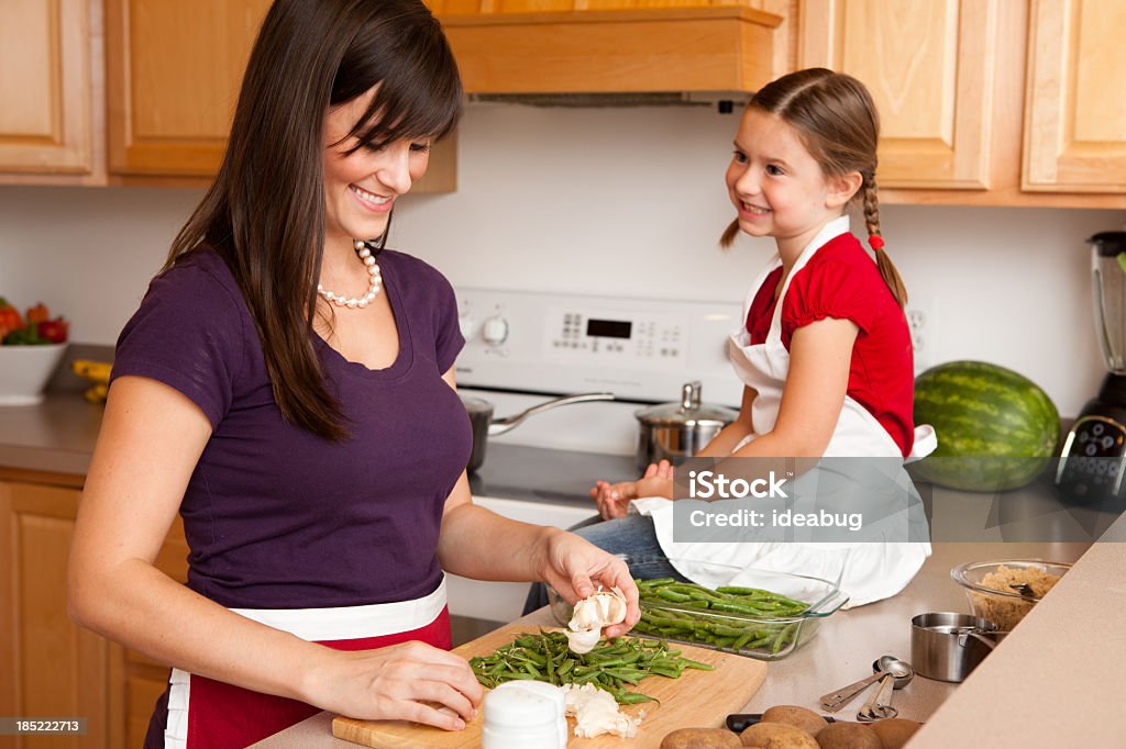 Happy Mother and Daughter Cooking in Their Kitchen at Home Color image of a happy, young mother and daughter cooking together in their kitchen at home. Kitchen Stock Photo