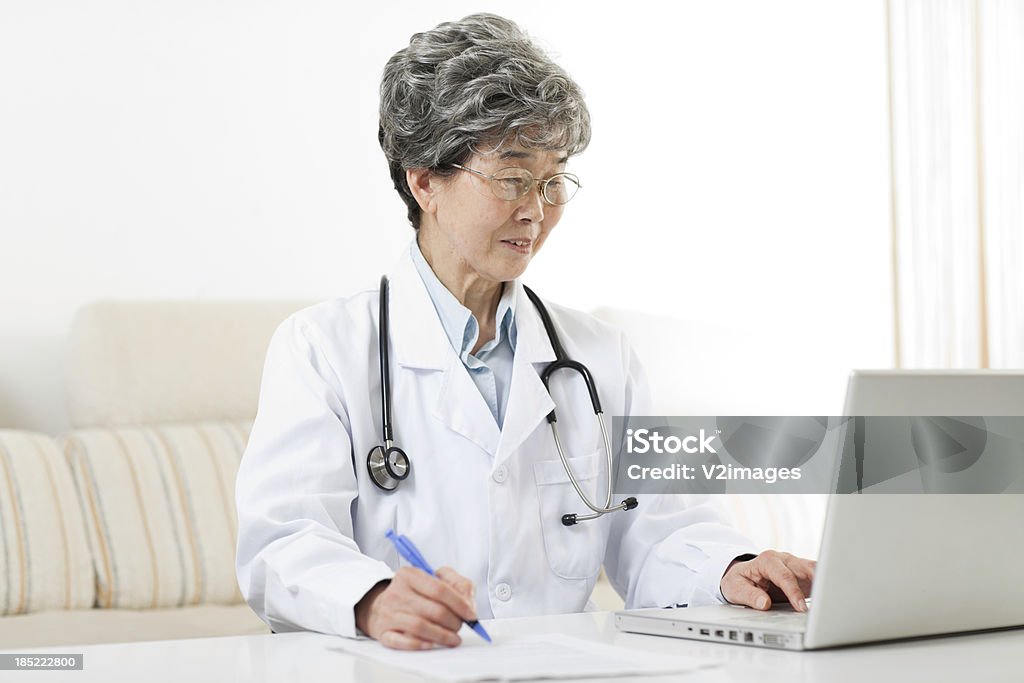 Doctora usando computadora portátil, llenado forma - Foto de stock de Doctor libre de derechos