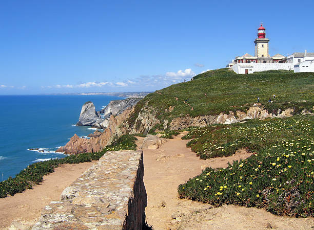 Cabo da Roca (Cape Roca) in Portugal with light house "Cabo da Roca (Cape Roca) is a cape. It forms the westernmost extent of mainland Portugal and continental Europe. On ground growing yellow sea fig (Carpobrotus edulis)," serra de sintra stock pictures, royalty-free photos & images