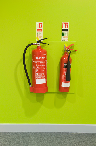Two fire extinguishers mounted on a bright green wall.