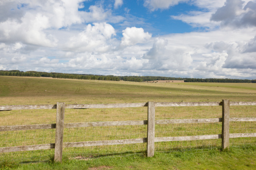 Horizontal image of wooden fence in front of open fields on the Salisbury Plain in Southeastern England.  A typical Salisbury cloudscape can be seen in the top half of the image.