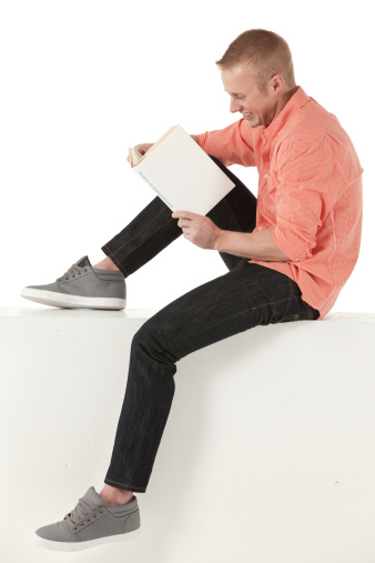 Man sitting on the ledge of wall reading a book