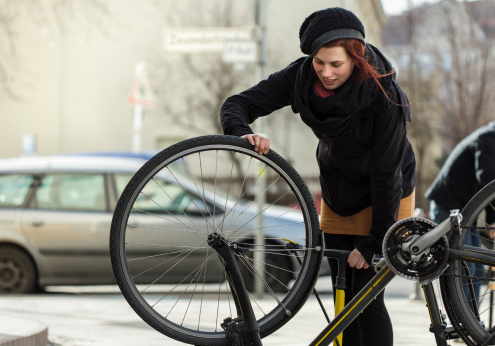 Woman commuter on a Berlin street with a flat tire on her Bicycle. She is pumping air into the tire after repairing the tire. Horizontal shot.