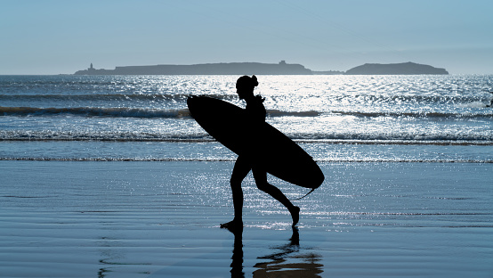Silhouette of an unidentified man with a surf board, walking in the beach of Essaouira, Morocco, which offers a perfect blend of wind and waves, attracting surf enthusiasts from around the world