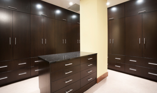 Modern large master bedroom walk-in closet with granite topped center island and floor to ceiling custom cabinets.