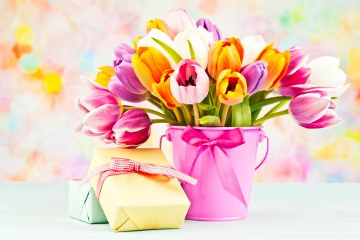 Beautiful bunch of tulips in pink pail with two wrapped gifts.