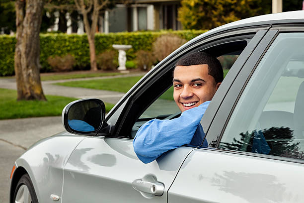 Young Man Behind The Wheel "Photo of a young man behind the wheel of his silver sports car, looking out of the window with a smile." teenager boy driving stock pictures, royalty-free photos & images