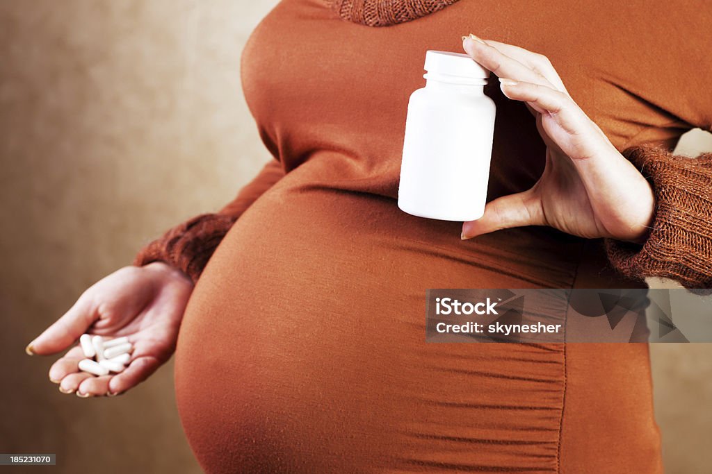 Donna incinta holding pillole. - Foto stock royalty-free di Accudire