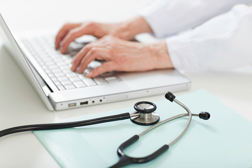 Doctor's hands using laptop at desk, stethoscope with envelope in foreground