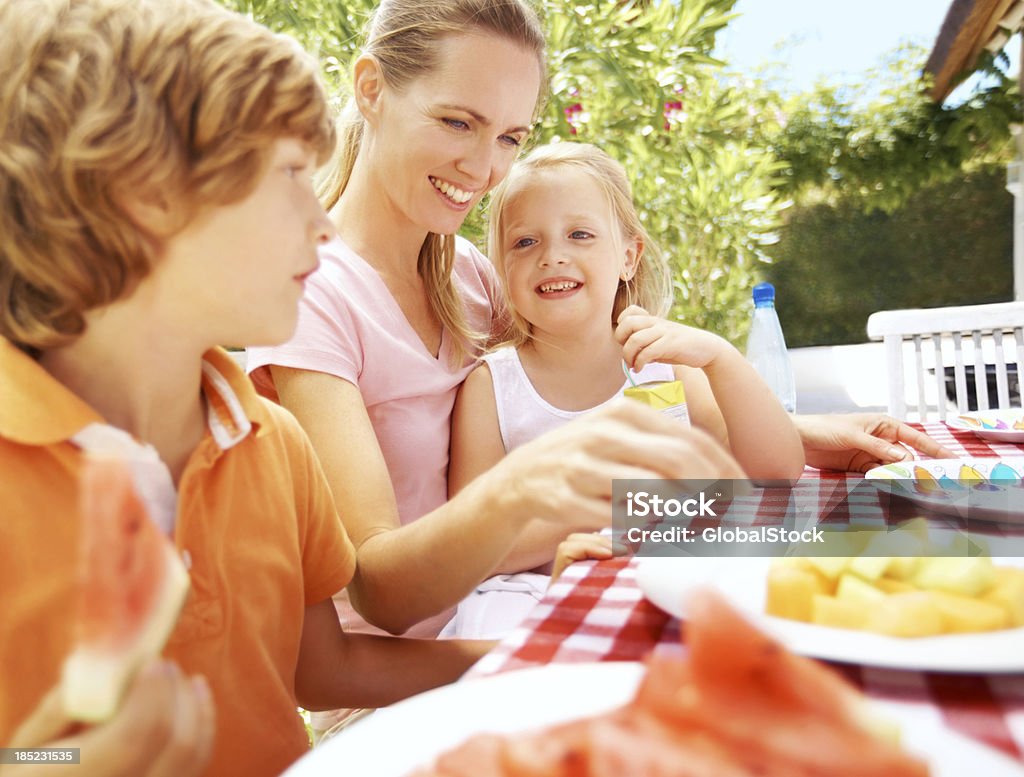 Mealtime with mum Two small children having a meal with their smiling young mother Adult Stock Photo