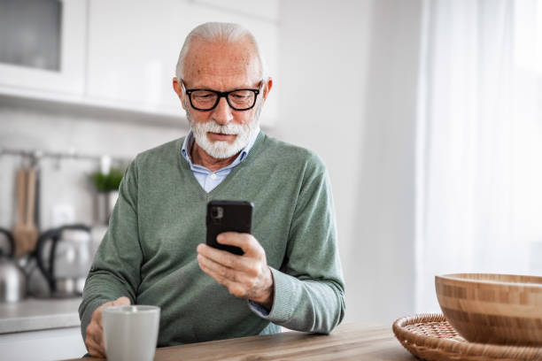 istock Old man, pensioner, sitting in kitchen with happy smile drinking hot coffee or tea and using mobile phone, morning routine, carefree retirement days 1852316935