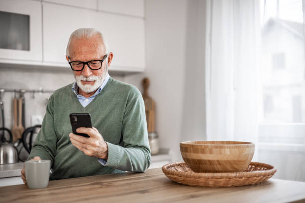 istock Old man, pensioner, sitting in kitchen with happy smile drinking hot coffee or tea and using mobile phone, morning routine, carefree retirement days 1852316936