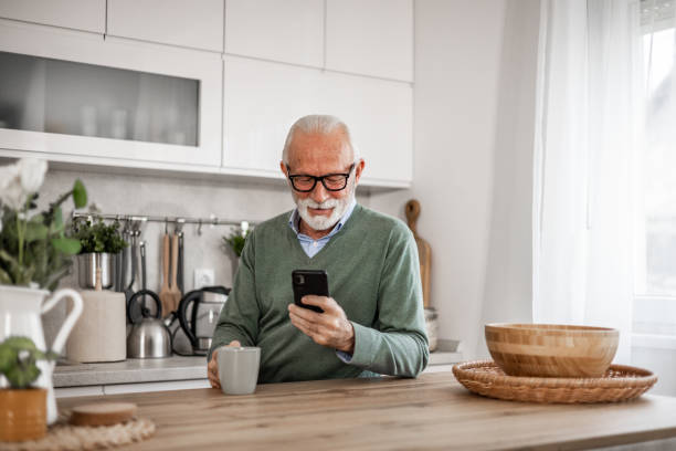 istock Old man, pensioner, sitting in kitchen with happy smile drinking hot coffee or tea and using mobile phone, morning routine, carefree retirement days 1852317056