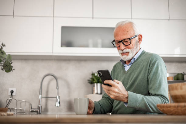 istock Old man, pensioner, sitting in kitchen with happy smile drinking hot coffee or tea and using mobile phone, morning routine, carefree retirement days 1852318006