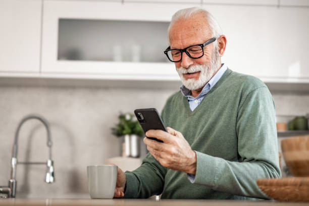 istock Old man, pensioner, sitting in kitchen with happy smile drinking hot coffee or tea and using mobile phone, morning routine, carefree retirement days 1852318015