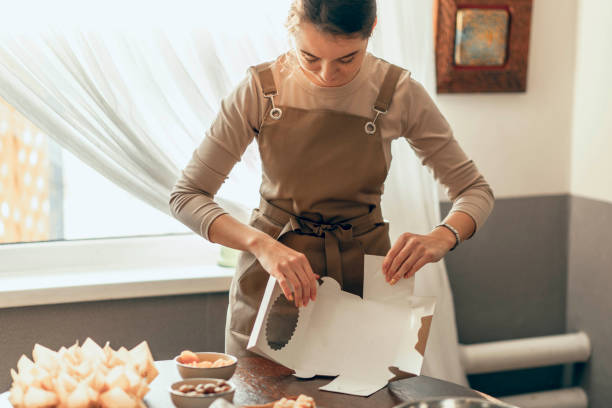 istock Happy woman bakery shop owner holding delivery box for customer order. Bakery chef baking pastry and cake in the kitchen. Small business entrepreneur and food delivery concept. 1852319087