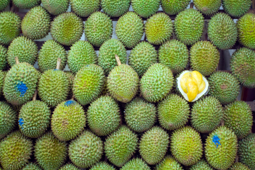 Stacked fruit and socalled Singaporean King of fruits Durian. Night shot. Fruit is quite tasting very strong and popular one for real Singaporean people. For foreigners mostly to strong smelling and tasting. One fruit is opened to see inner yellow pulp. Fruit is only available around Singapore and Maylasia.