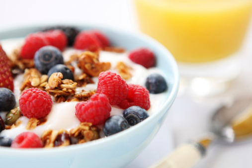 Granola with oatmeal, hazelnuts, kiwis, blueberries and yogurt in white bowl on light background