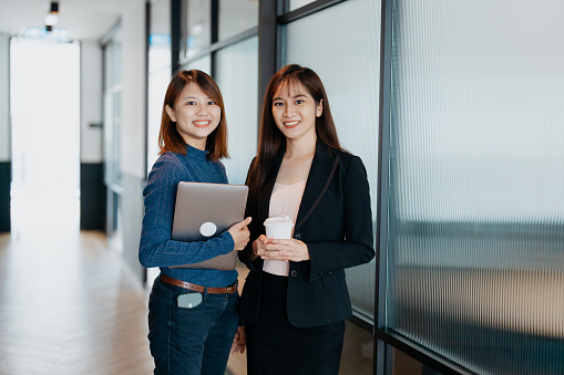 Portrait of two Asian Chinese Businesswomen smiling and looking at camera in a modern office
