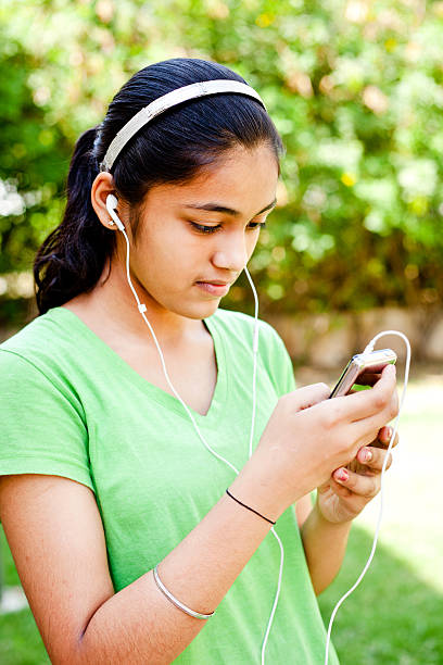 Cheerful Casual Indian Teenage Girl Listening Music Cheerful Casual Indian Teenage Girl Listening Music on MP3 Player 13 14 years child teenage girls lying down stock pictures, royalty-free photos & images