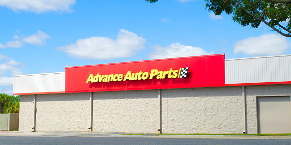 Advance auto car parts store, Ocala, Florida USA - October 22, 2023   Exterior view bright yellow letters on red with checkered flag logo.  Bright blue sky background on sunny day.  Side of building