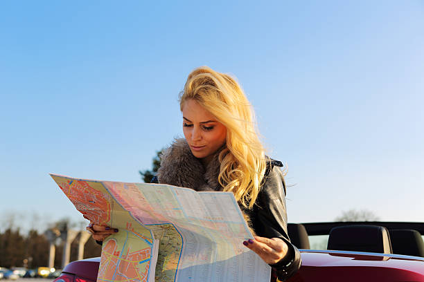 istock Young woman sitting on back of car,looking at map 185234253