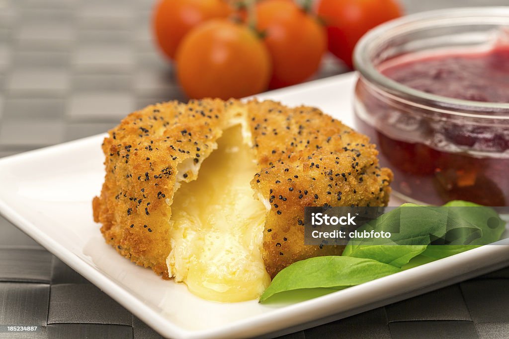 Baked Camembert with cranberry sauce A handmade Camembert cheese covered with poppy seeds and breadcrumbs that has been baked and served with cranberry sauce. Baked Stock Photo
