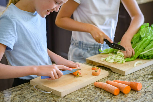 deux belles jeunes filles coupant des légumes dans une cuisine en gros plan - carrot close up silverware cutting board photos et images de collection