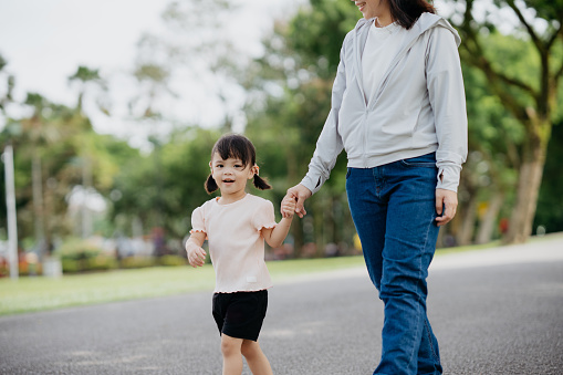 Young asian girl holding hand of her mother and walking in public park