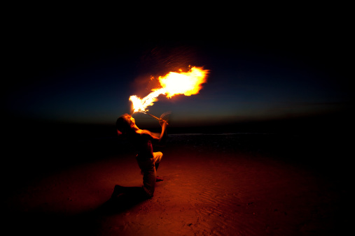 Fire eater performance in the beach against blue and dark sky