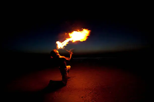 Fire eater performance in the beach against blue and dark sky