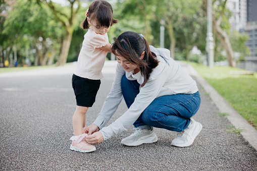 Mother putting on shoe for young daughter in public park
