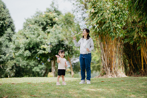 Young asian girl blowing and playing soup bubbles with her mother at public park