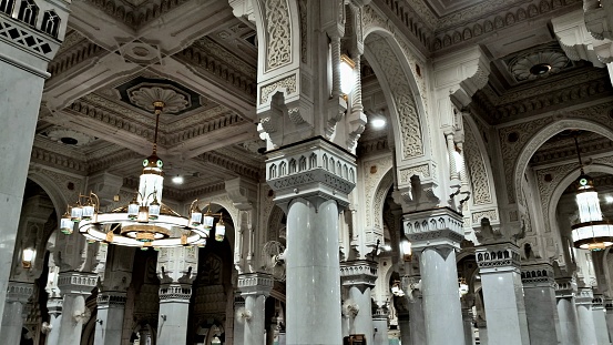 A beautiful view of the interior design of Al-Masjid Al-Haram with the the decorative details of the pillar and the luxurious chandeliers.
