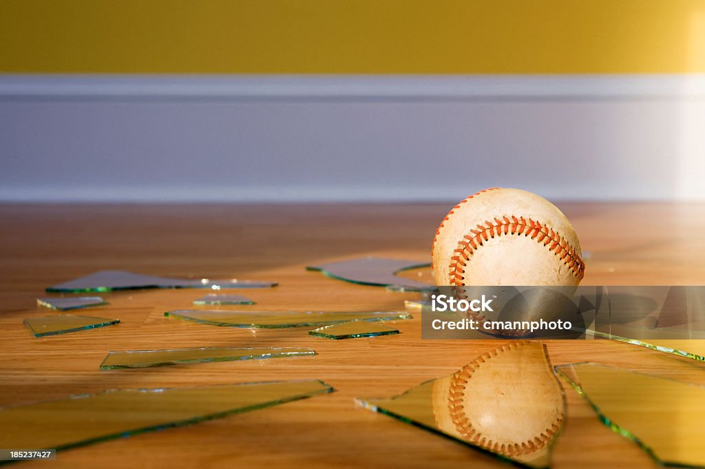 Baseball with Broken Window glass on wood floor Baseball - Broken Window. A baseball sitting on an oak laminate floor with broken pieces of glass from a window pane, as the sunlight shines across the floor and wall. Breaking Stock Photo