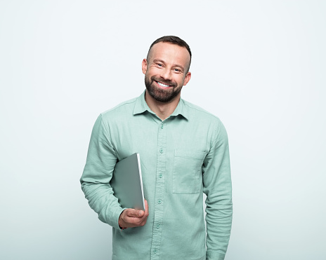 Handsome mid adult men wearing green shirt holding laptop in hand and smiling at camera. Studio shot, white background.