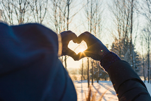 Woman making heart symbol with hands wearing gloves, sunny winter evening, sunrays, Valentines day, Love concept.