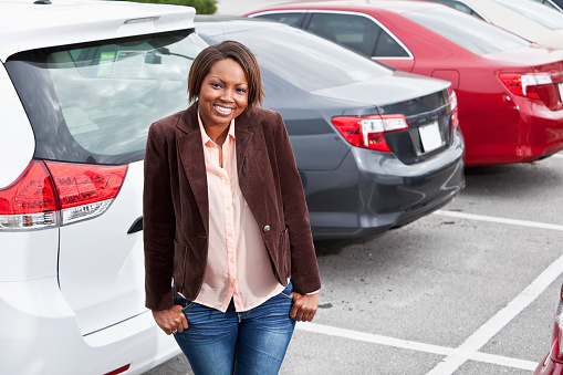 African American woman (30s) standing in parking lot.  Shallow DOF, focus on foreground.