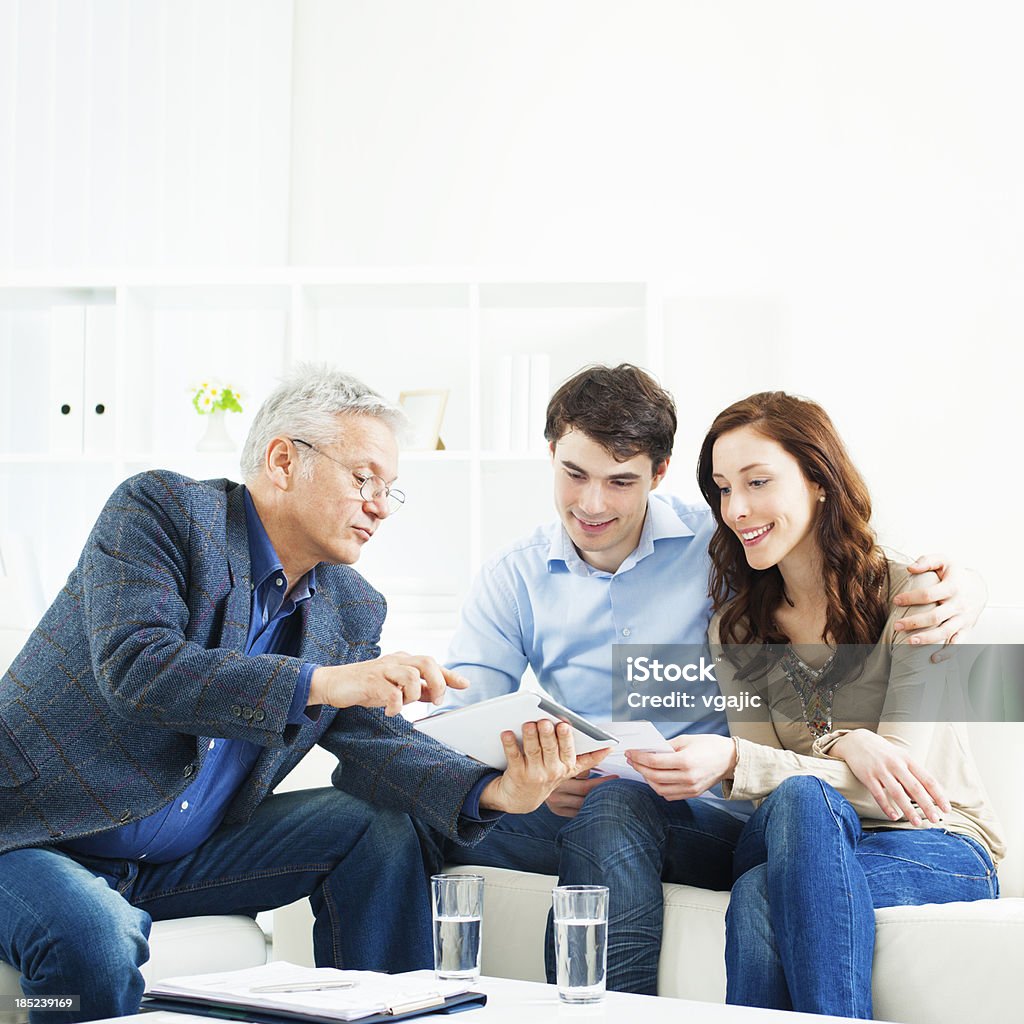 Couple Meeting With Financial Advisor Young Couple Meeting With Senior Financial Advisor presenting new bank offers and investments on digital tablet PC. Senior Financial Advisor pointing with hand to some new offers. Banking Stock Photo