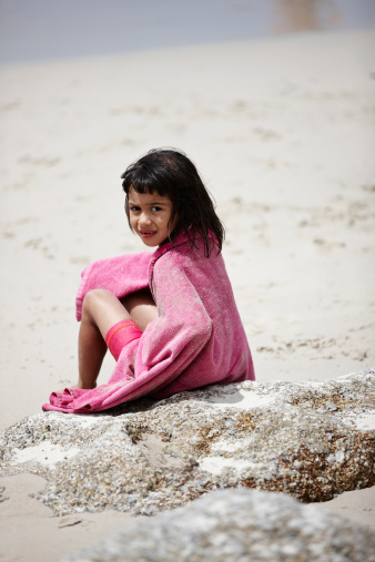 Six year old girl sitting on the beach wrapped in towel