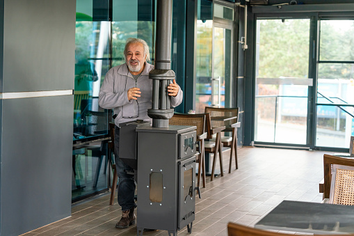 Coffee Meetup in Their 70s. Energetic 70-Year-Old Man Warming by a Stove