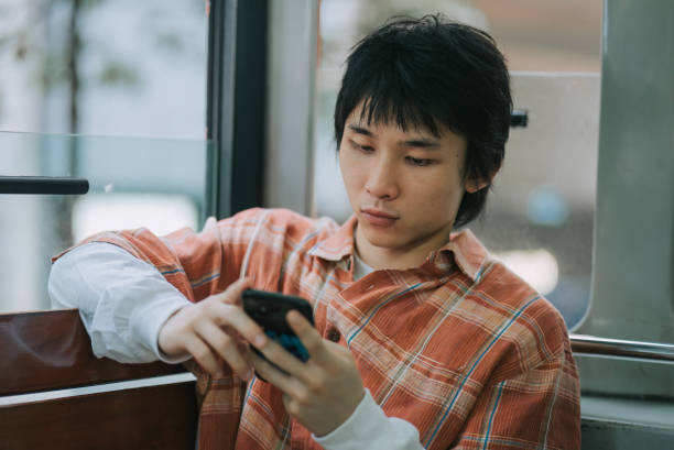 istock Asian Chinese young man using smart phone text messaging sitting in double-decker bus in Hong Kong Island alone 1852393619