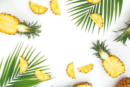 Tropical frame made of sliced pineapple and palm leaves on white background. Flat lay, top view.