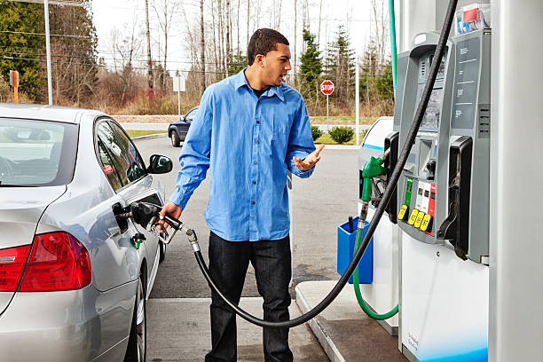 Gas Station Frustration "Photo of a young man watching filling his gas tank, watching in disbelief as the dollar amount climbs on the gas pump display too quickly to comprehend." refueling stock pictures, royalty-free photos & images
