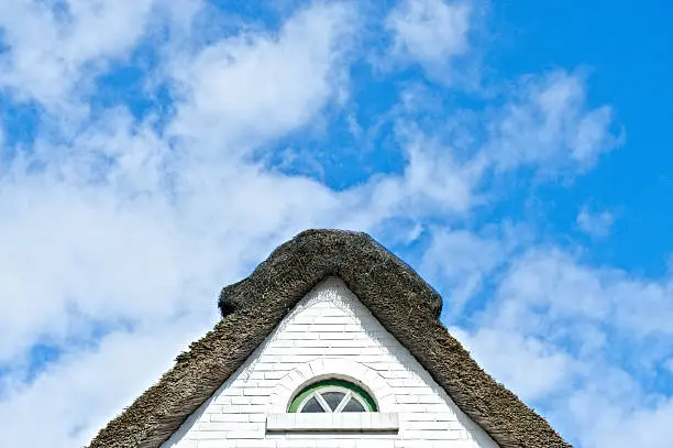 Home with traditional straw roof in front of a blue sky, with beautiful clouds