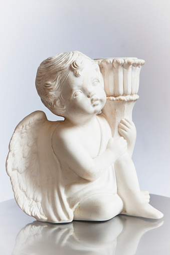 White small statue of sitting angel holding a torch with reflection, full frame vertical composition with copy space
