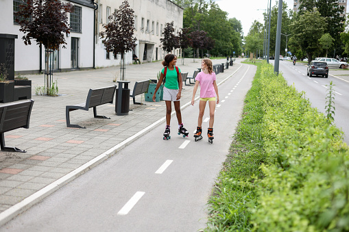 Two friends inline skating on a street. Both about 12 years old, African and Caucasian females.