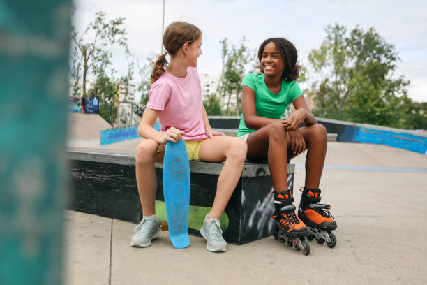 Two friends relaxing after skateboarding. Both about 12 years old, African and Caucasian females.