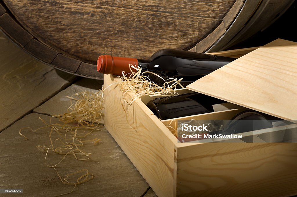 Wine Box in Cellar Close up of a wooden box of wine on a cellar floor with an oak barrel in the background. Wine Stock Photo
